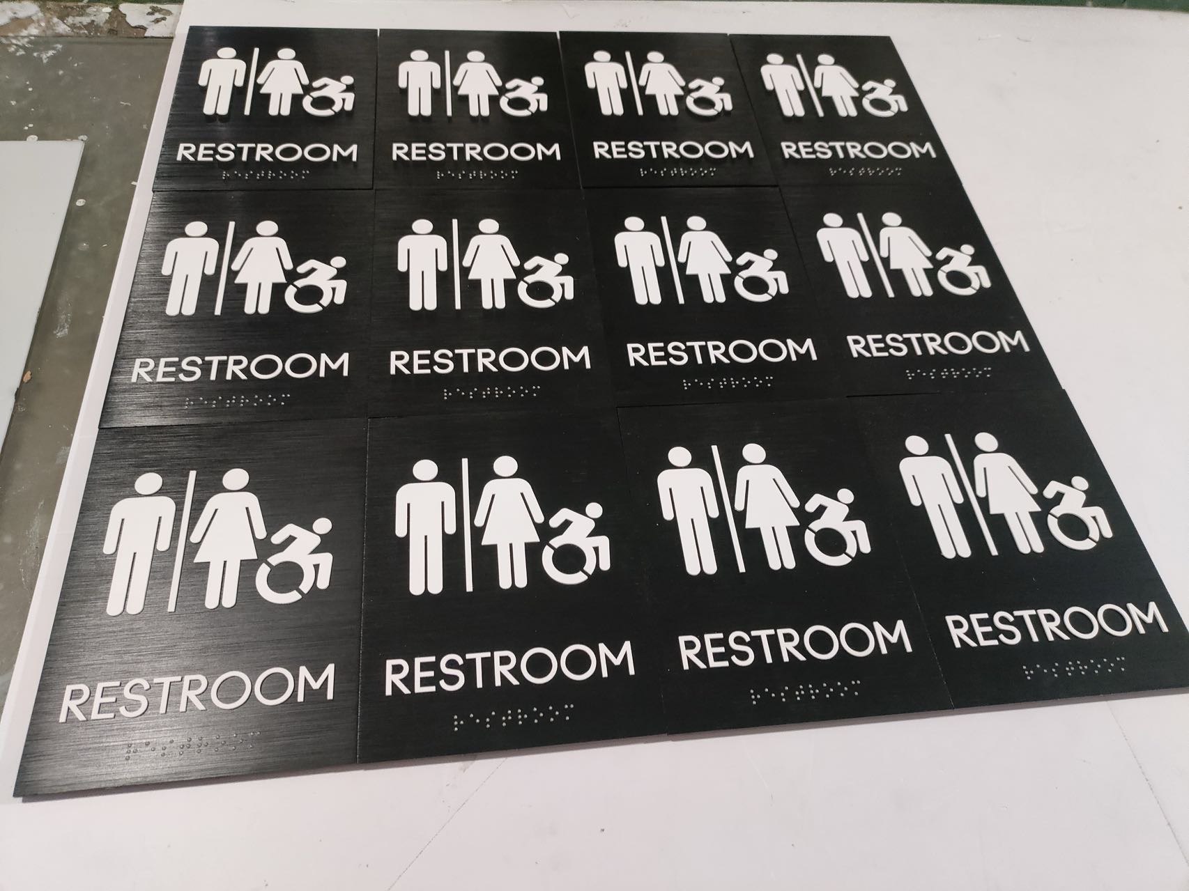 Batch of black accessible restroom signs with white pictograms, text and tactile Braille