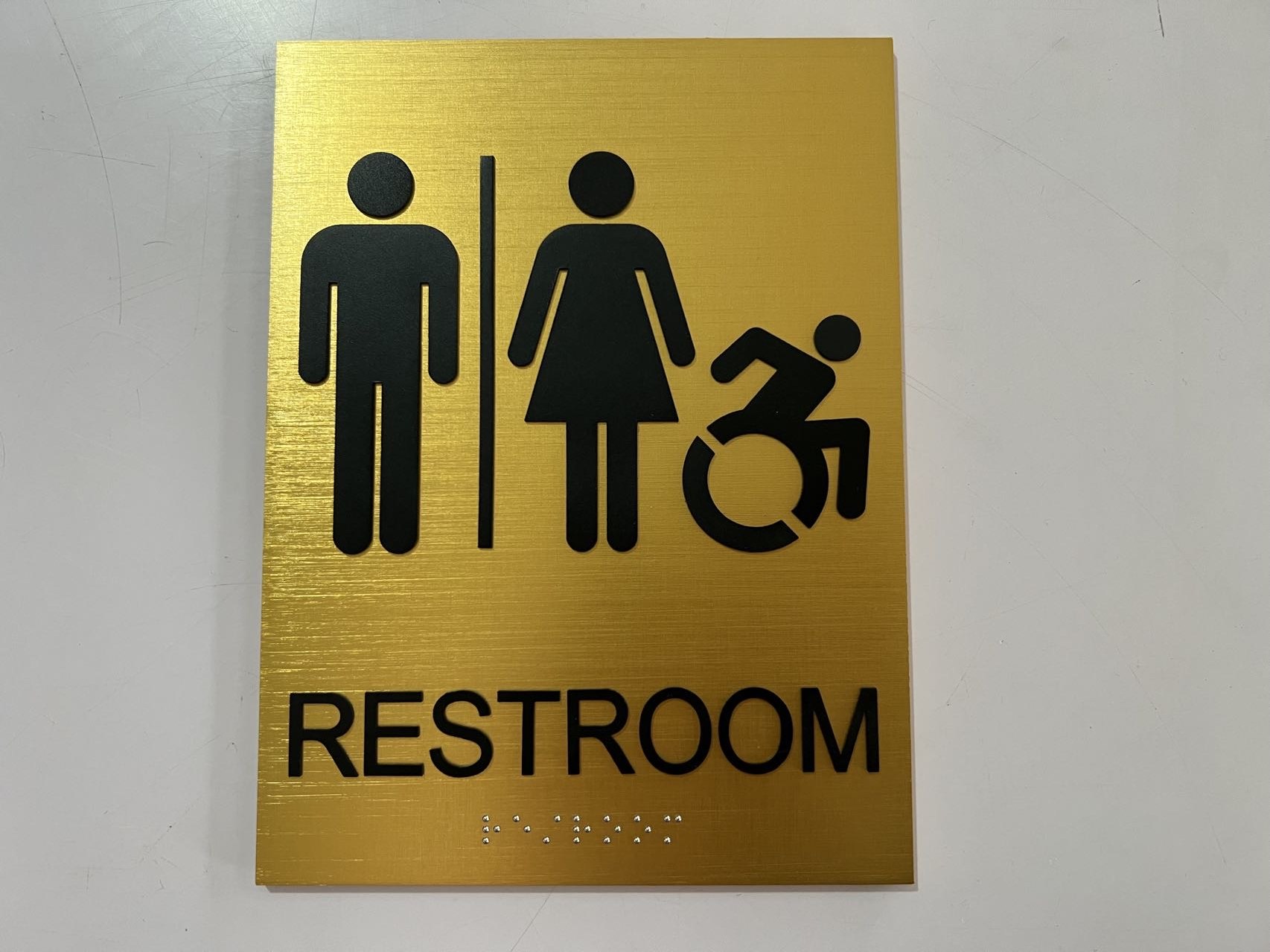 Front view of a brushed gold accessible restroom sign with male, female and wheelchair pictograms