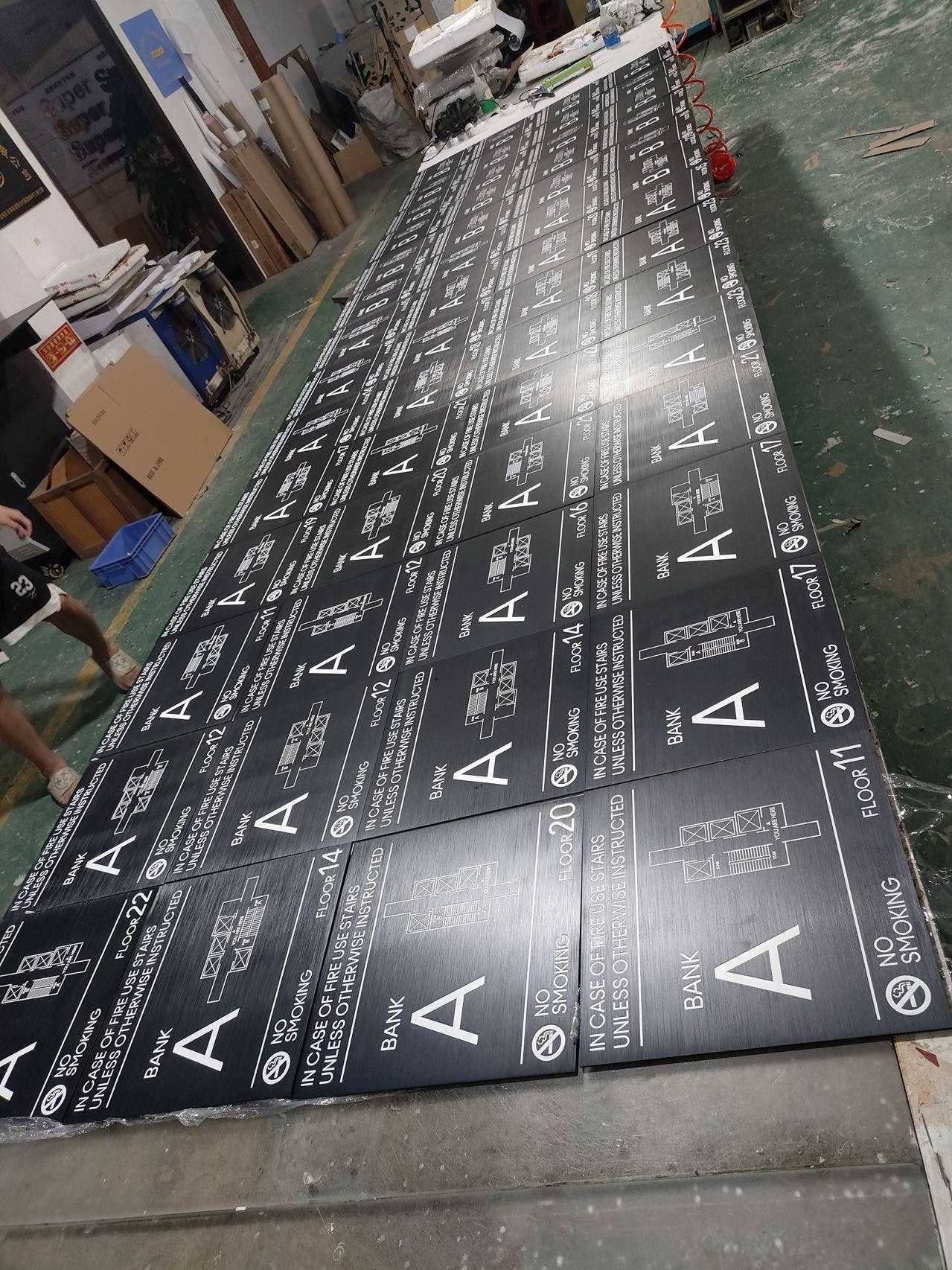 Batch of black floor-specific fire evacuation map signs arranged in a signage workshop