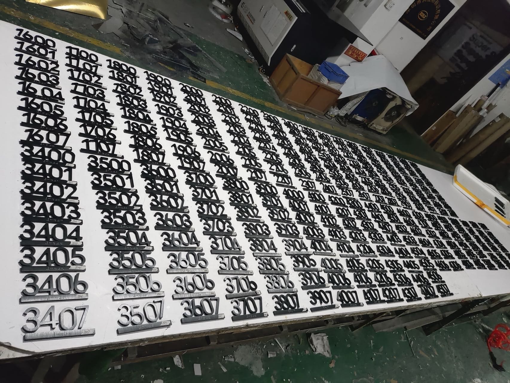Large production batch of black hotel room number signs arranged by floor in a signage workshop